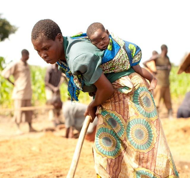 A Malawian mother lays the foundation of a buildOn school with her child on her back.