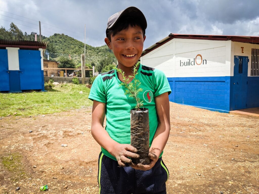 A boy in Guatemala helps plant trees outside his new buildOn school.