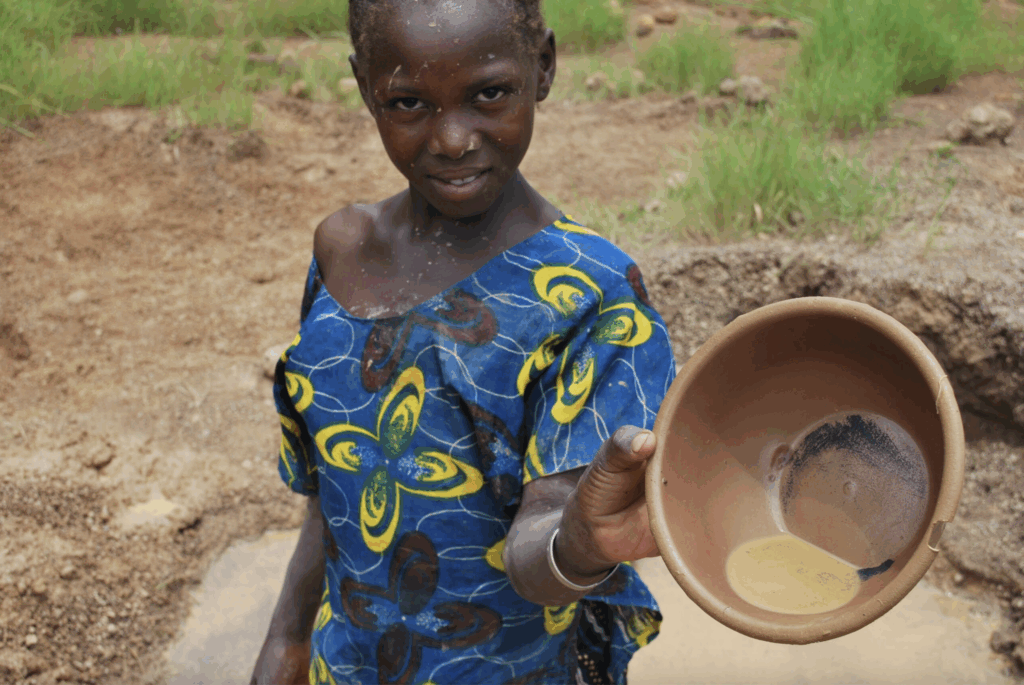 A girl holds up a pan used in artisanal gold mining. Source: SOMO