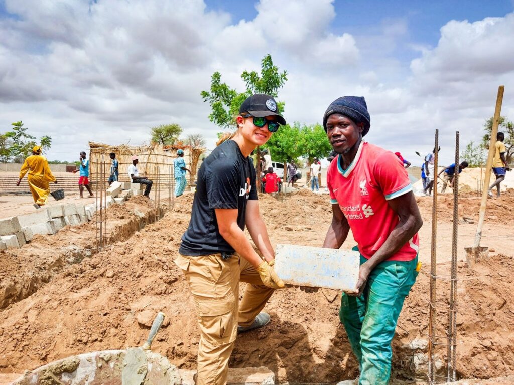 A Trek participant and a community member work together to lay bricks on the worksite in Senegal.